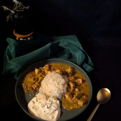A bowl of hearty chicken chili served over a bed of fluffy white rice, topped with a dollop of creamy sour cream, garnished with a sprinkle of fresh herbs.