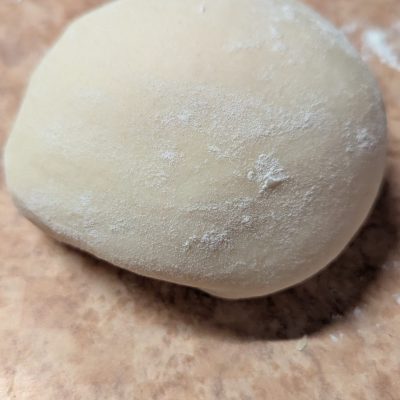 A smooth ball of homemade tortilla dough resting on a lightly floured surface, ready to be rolled out and cooked into fresh, soft tortillas.