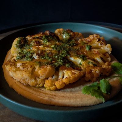 an-Fried Cauliflower with Cannellini Bean Purée & Cilantro Chimichurri A plate of golden pan-fried cauliflower resting on a creamy, seasoned cannellini bean purée, garnished with a vibrant cilantro-based chimichurri.