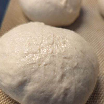 Freshly Baked Homemade Hamburger Rolls A tray of golden-brown, freshly baked Hamburger rolls resting on a sheet pan, their soft texture and fluffy interiors visible through slight cracks on the surface.