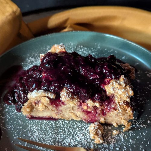 Oops! Bread Pudding with Blueberries & Powdered Sugar – A Sweet Mistake Worth Making A slice of Oops! Bread Pudding topped with a warm, thickened blueberry compote made from frozen blueberries, cornstarch slurry, lemon juice, cinnamon, and maple syrup, and lightly dusted with powdered sugar.