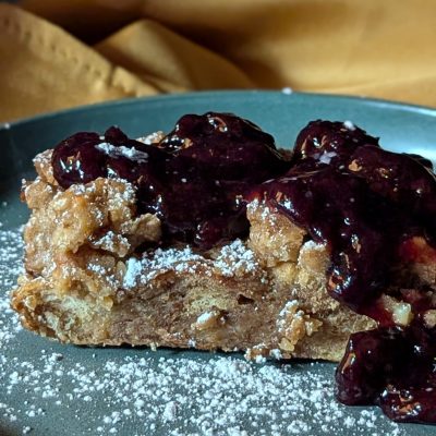 Bread Pudding with Amaretto Cherry Compote – A Cozy, Indulgent Treat A warm, golden-brown bread pudding fresh out of the oven, topped with a glossy amaretto cherry compote and a dusting of powdered sugar. The rich, syrupy cherries contrast beautifully with the soft, custardy bread.
